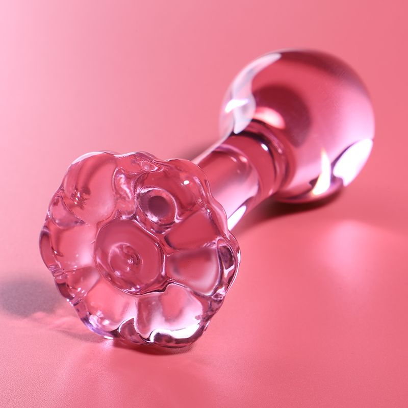 Plug anale in vetro rosa con base dettagliata a forma di fiore su sfondo rosa.