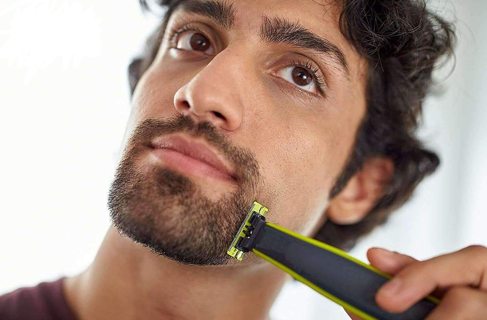Uomo che si rade con un regolabarba nero-giallo. Barba visibile.