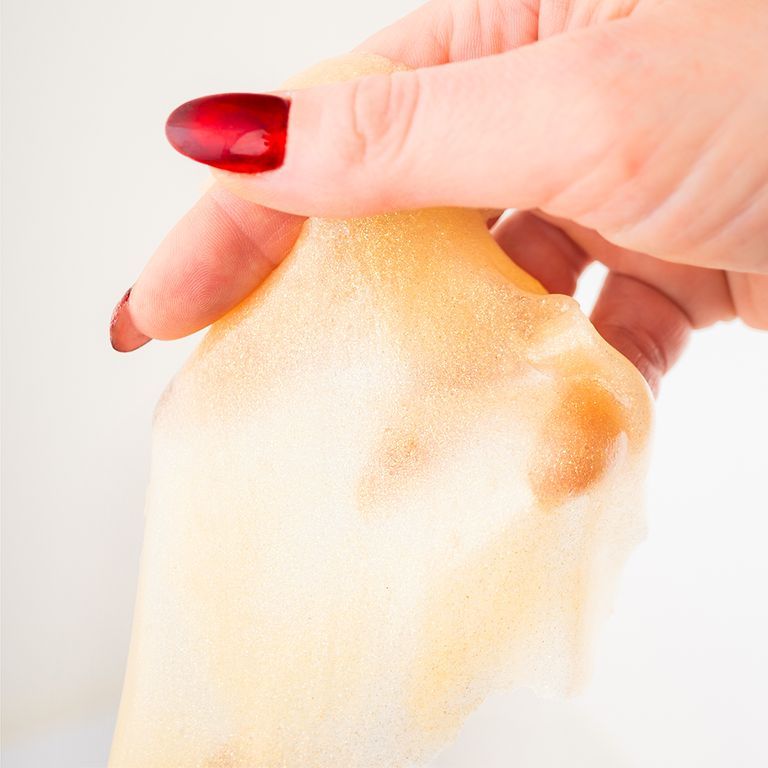 Mano che tiene una maschera per il viso. Gialla. Unghie rosse. Sfondo bianco.