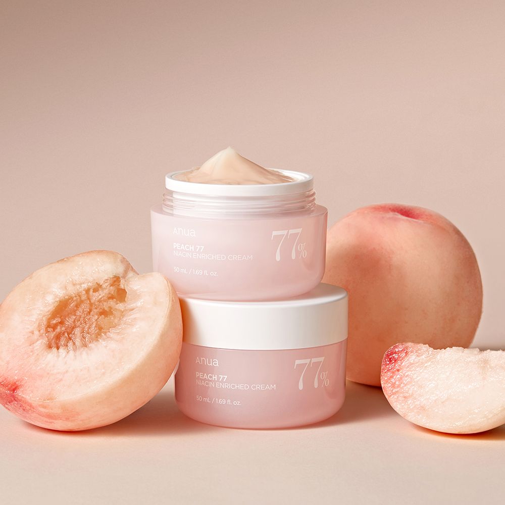 Due vasetti di crema arricchita alla niacinamide ANUA Peach 77%, circondati da pesche fresche.