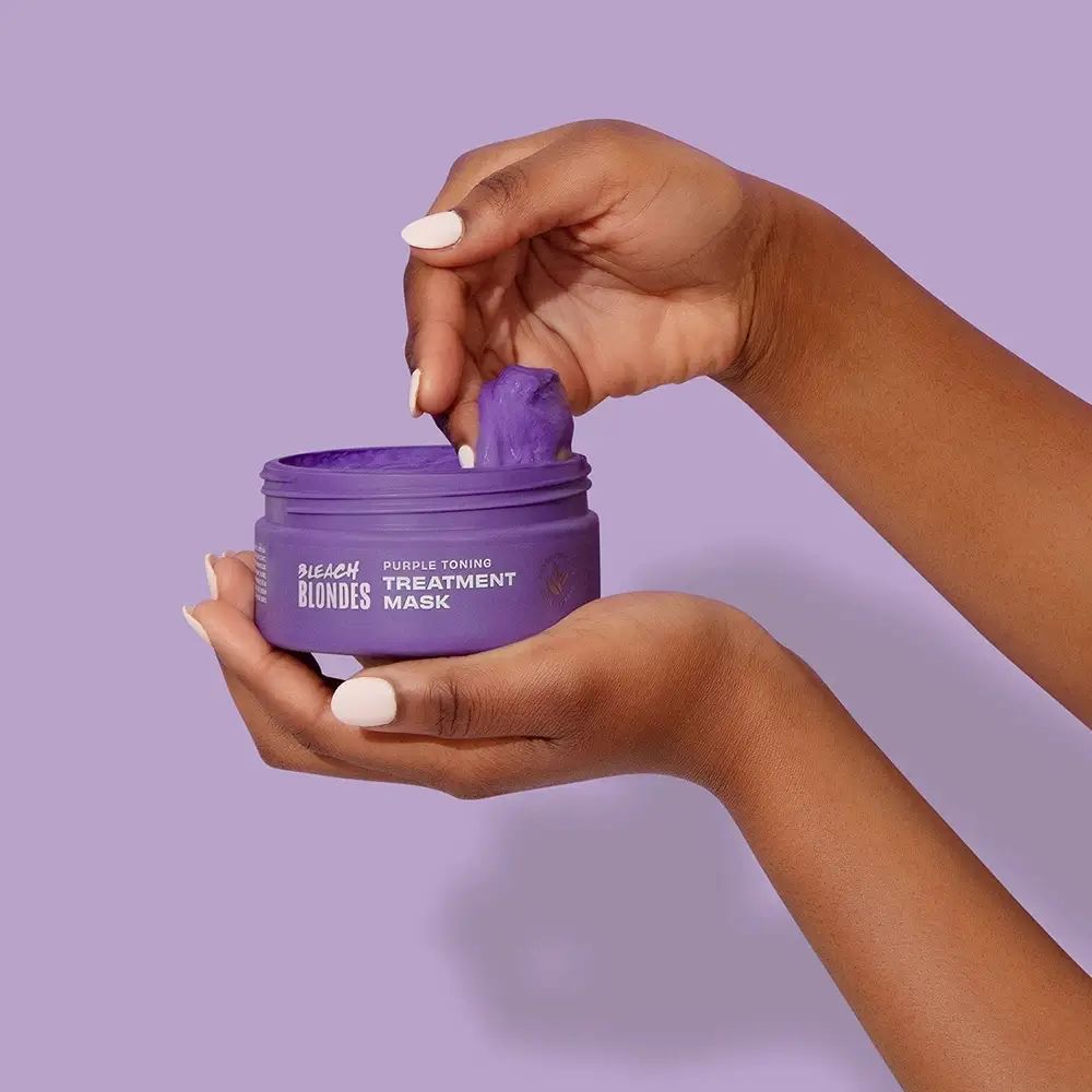 Mani che tengono un vaso viola aperto. Prodotto: Bleach Blondes Purple Toning Treatment Mask. Prodotto viola visibile.