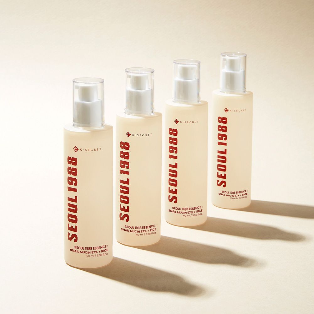 Quattro flaconi K-SECRET Seoul 1988 Essence. Flaconi beige con scritta rossa, allineati.