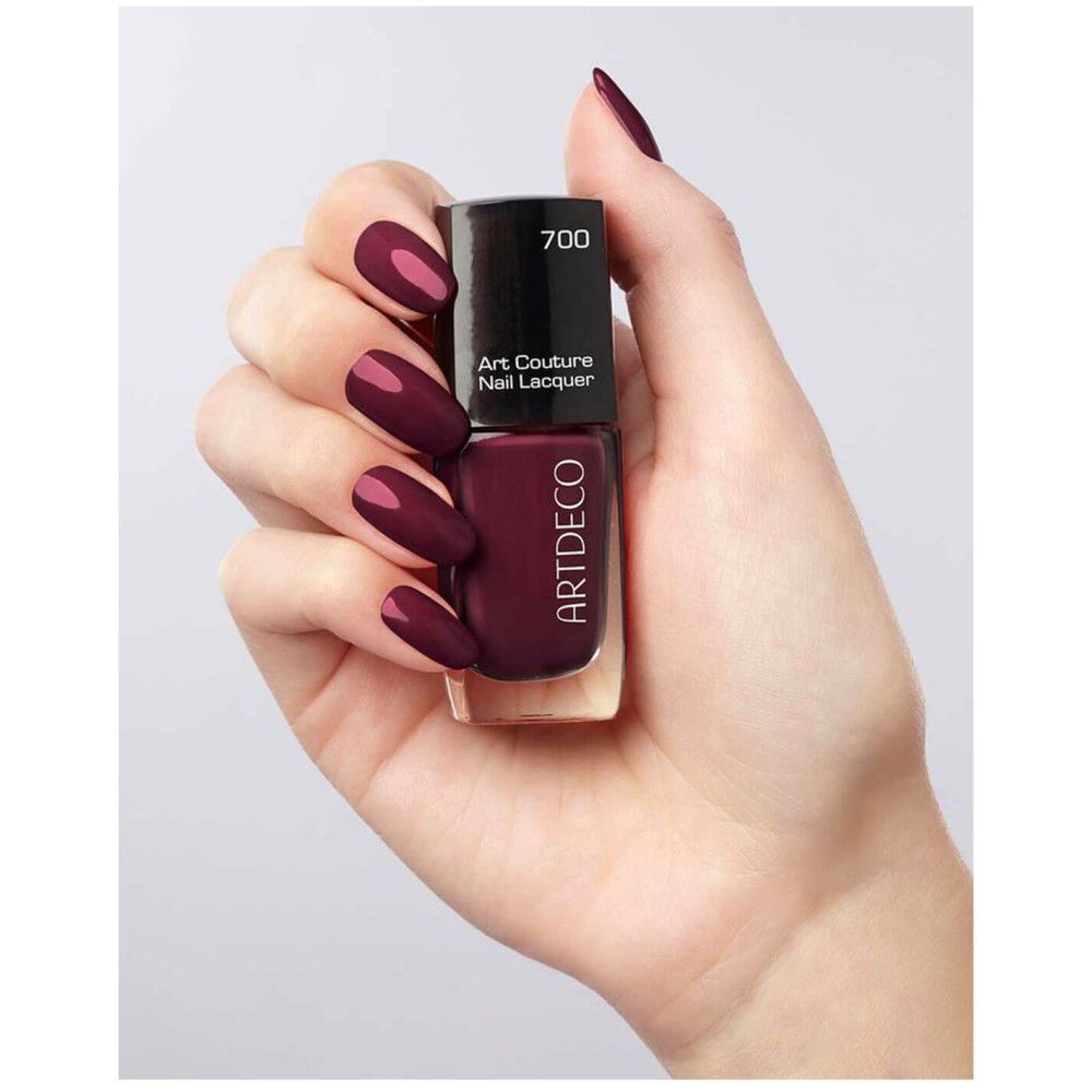Flacone di smalto Artdeco, rosso scuro. Scritta: Art Couture Nail Lacquer. Bottiglia tenuta in mano.