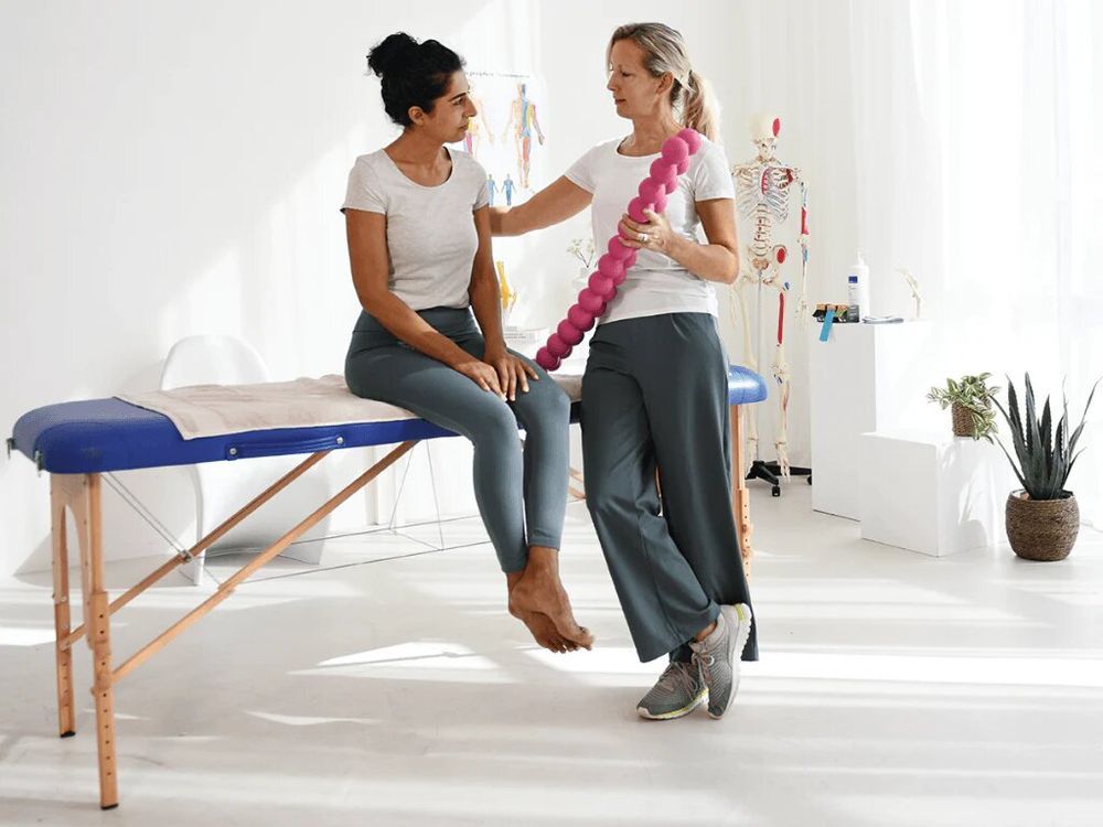 Donna tiene SPINEFITTER® rosa. Due donne in una sala di trattamento. Una è seduta su un lettino.