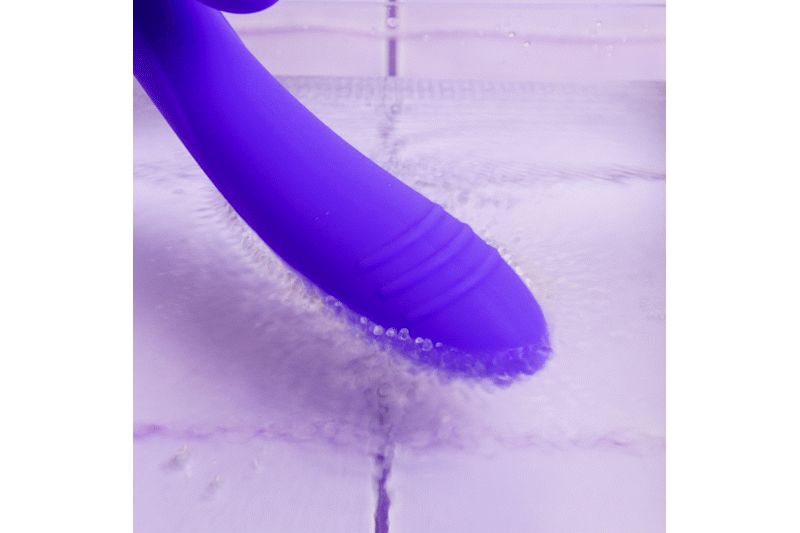 Vibratore viola sott'acqua. L'estremità del vibratore è visibile, circondata dall'acqua. L'acqua scorre sulla superficie.