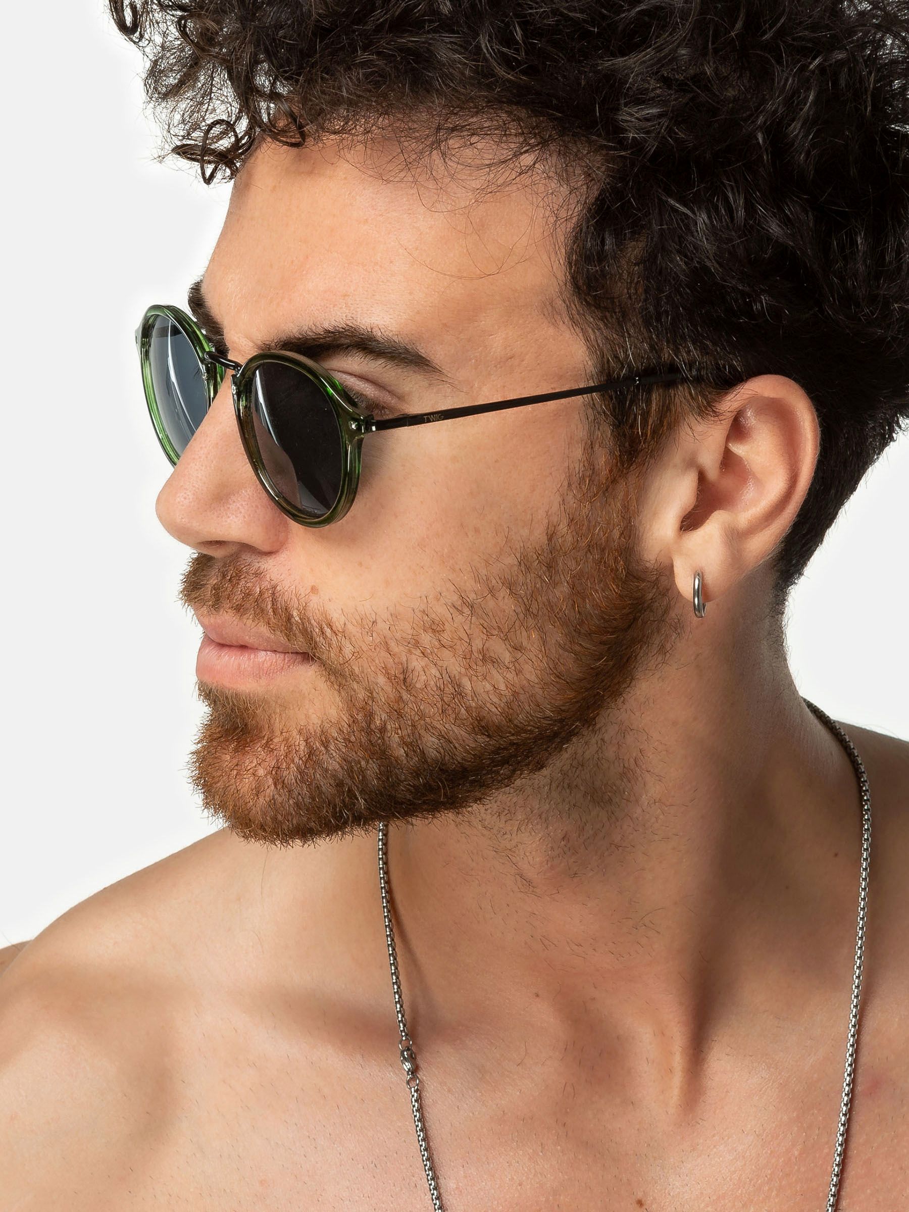 Primo piano di un uomo con occhiali da sole verdi. Lenti rotonde, aste nere. Marchio Twig.