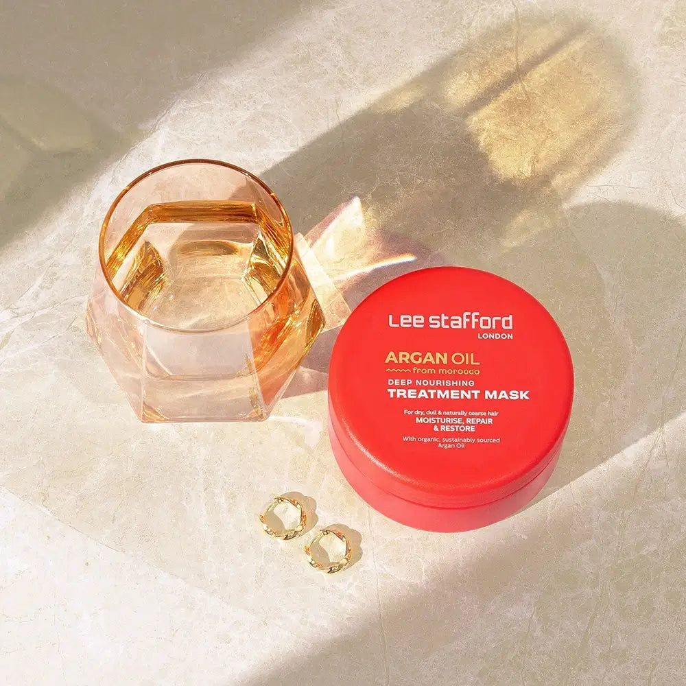 Vasetto rosso Lee Stafford Maschera Trattamento Nutriente Profondo all'Olio di Argan vicino a un bicchiere.