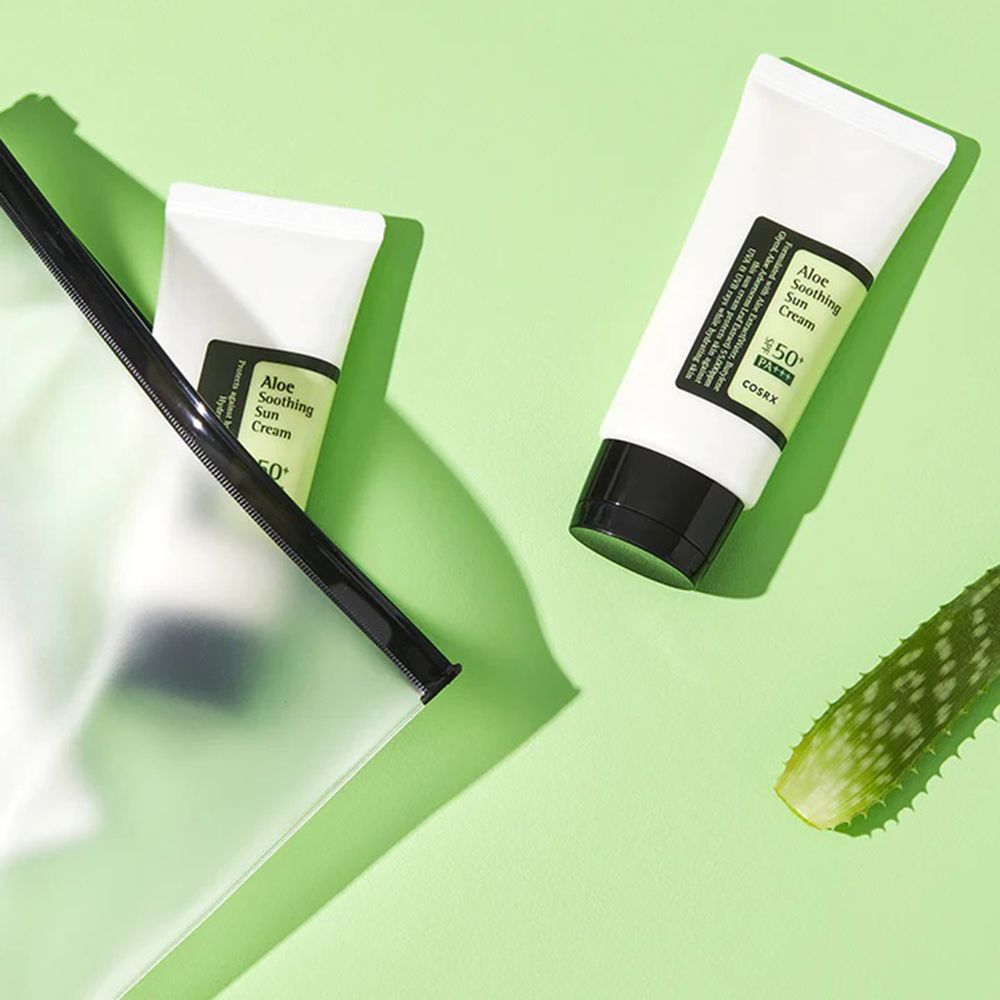 Due tubi bianchi e neri con scritta: Aloe Soothing Sun Cream, COSRX. Su sfondo verde.