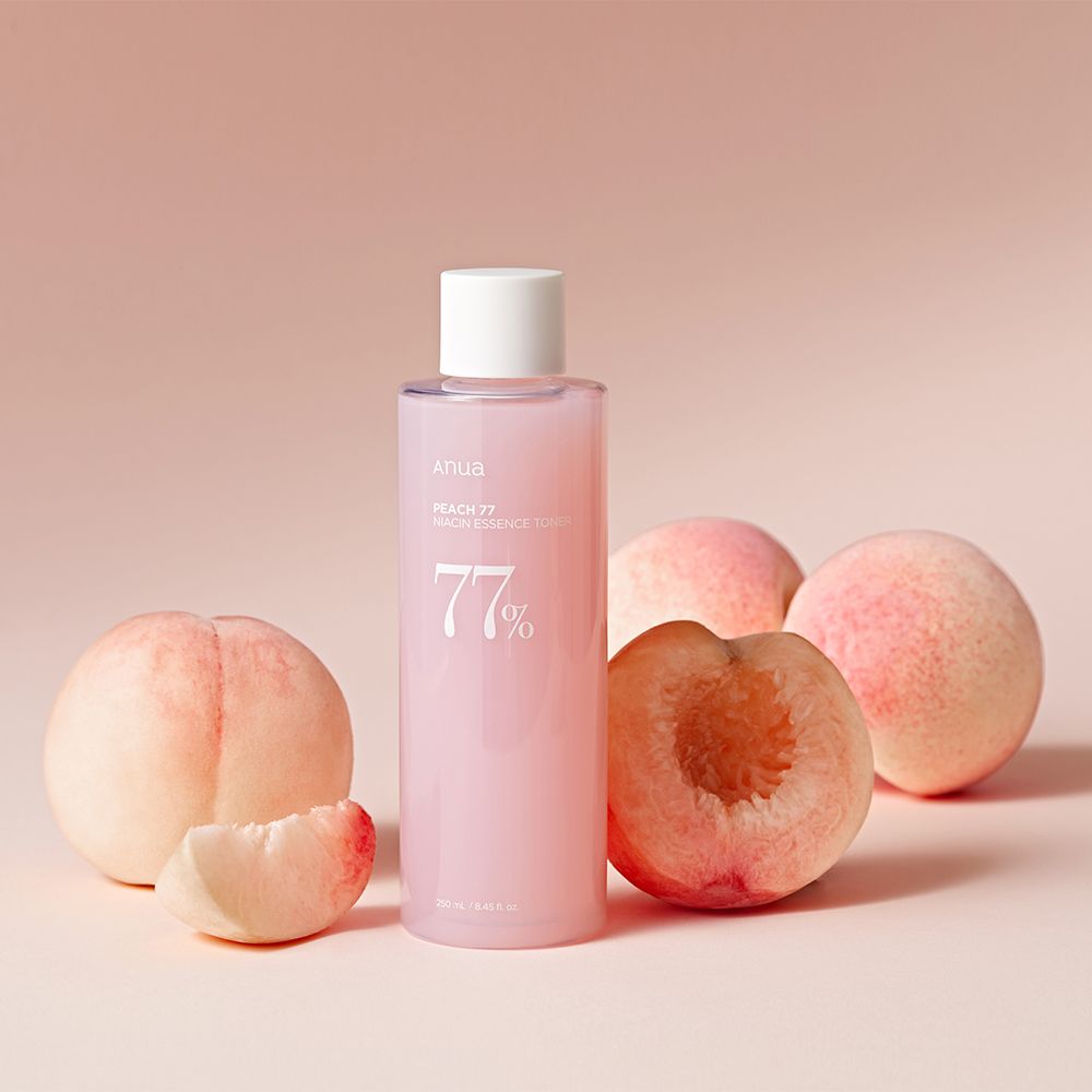 Bottiglia di tonico essenza niacinamide ANUA Peach 77% circondata da pesche.