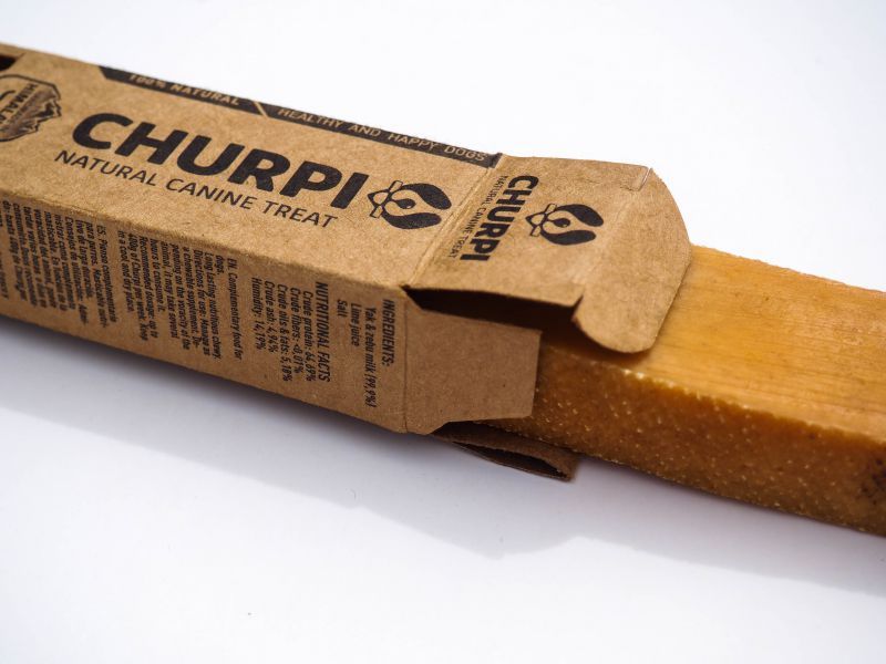 Churpi snack masticabile in confezione di cartone aperta. Nome prodotto e testo. Naturale.