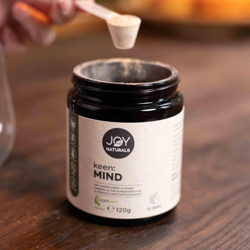 Barattolo marrone di polvere JOY NATURALS keen:MIND. Un cucchiaio è tenuto sopra. Scritta: 120g.
