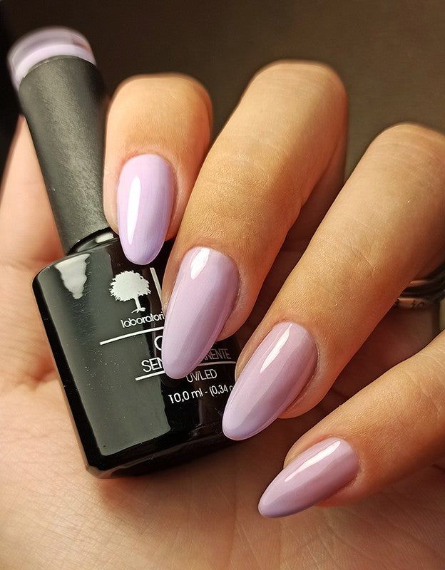 Mano con unghie lilla. Flacone di smalto accanto. Unghie di forma ovale, lucide.