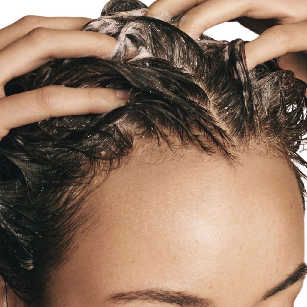 Primo piano di mani che lavano i capelli con schiuma. Visibili: cuoio capelluto, capelli e mani.