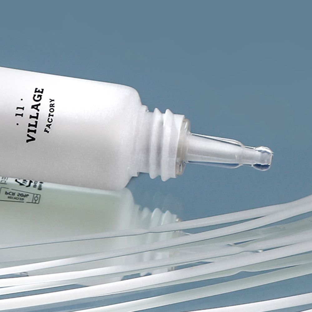 Tubo bianco, chiusura marrone, punta trasparente. Scritta nera: VILLAGE 11 FACTORY. Su superficie liscia.