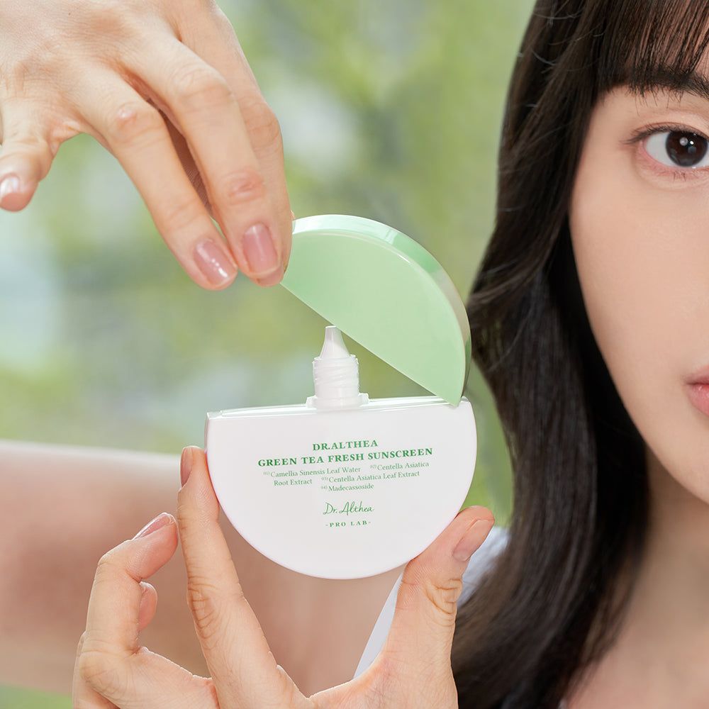 Persona che tiene un prodotto di crema solare semiaperto. Coperchio verde, contenitore bianco con testo. Volto di una persona sullo sfondo.