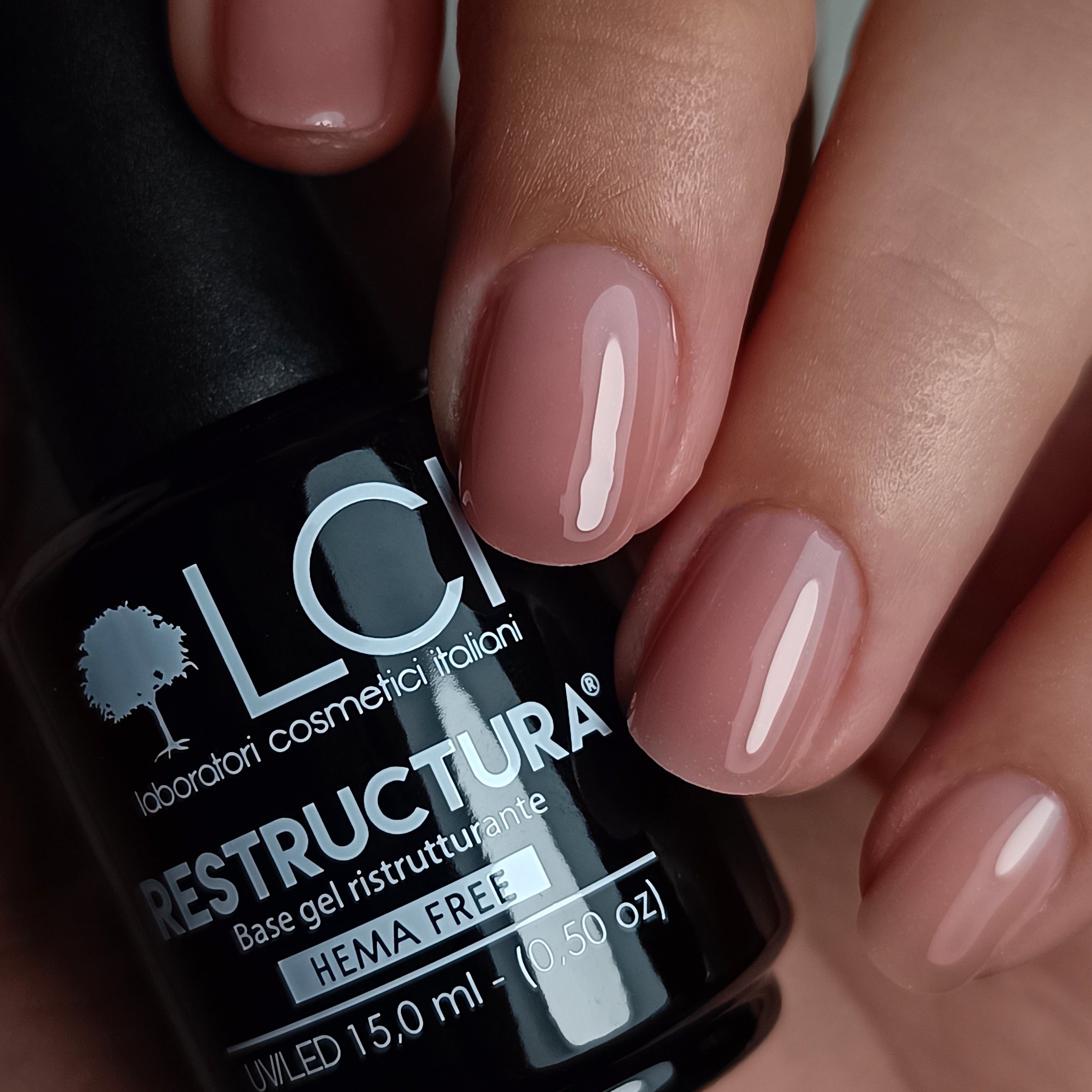 Flacone di smalto accanto a unghie smaltate. Scritta: Restructura Base Gel, HEMA Free, 15,0 ml.