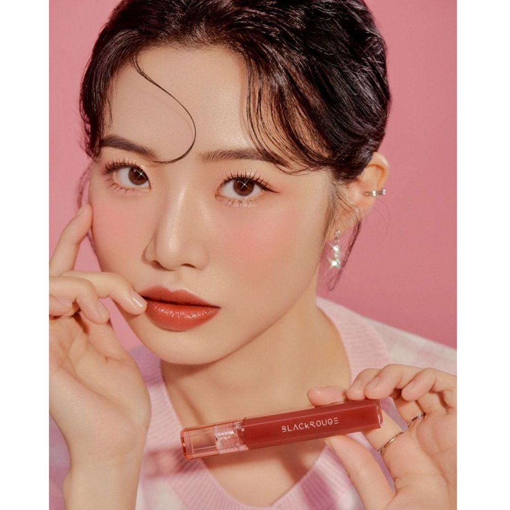 Donna con rossetto. Tiene in mano un rossetto con la scritta "BLACKROUGE". Sfondo rosa.