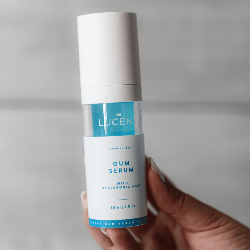 Flacone di siero gengivale tenuto in mano. Bianco e blu. Scritta: GUM SERUM, Be Lucent. Con acido ialuronico. 30ml/1 fl oz.