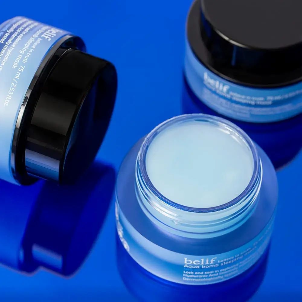 Tre vasetti blu di Belif Aqua Bomb Sleeping Mask. Un vasetto è aperto, il prodotto è visibile. Coperchi neri.