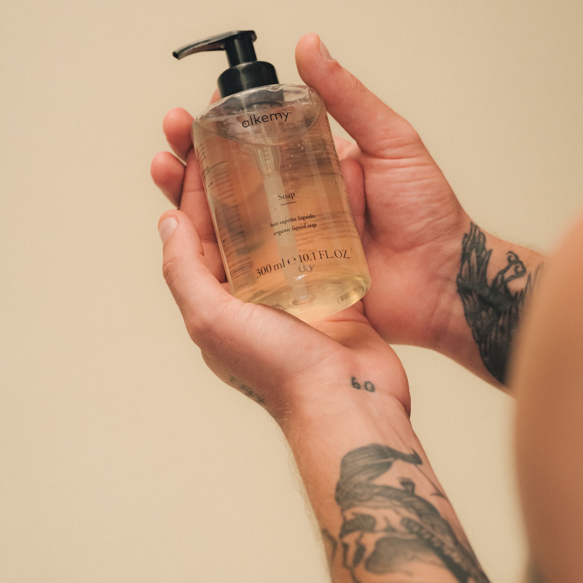 Mani tatuate tengono flacone di sapone liquido trasparente.