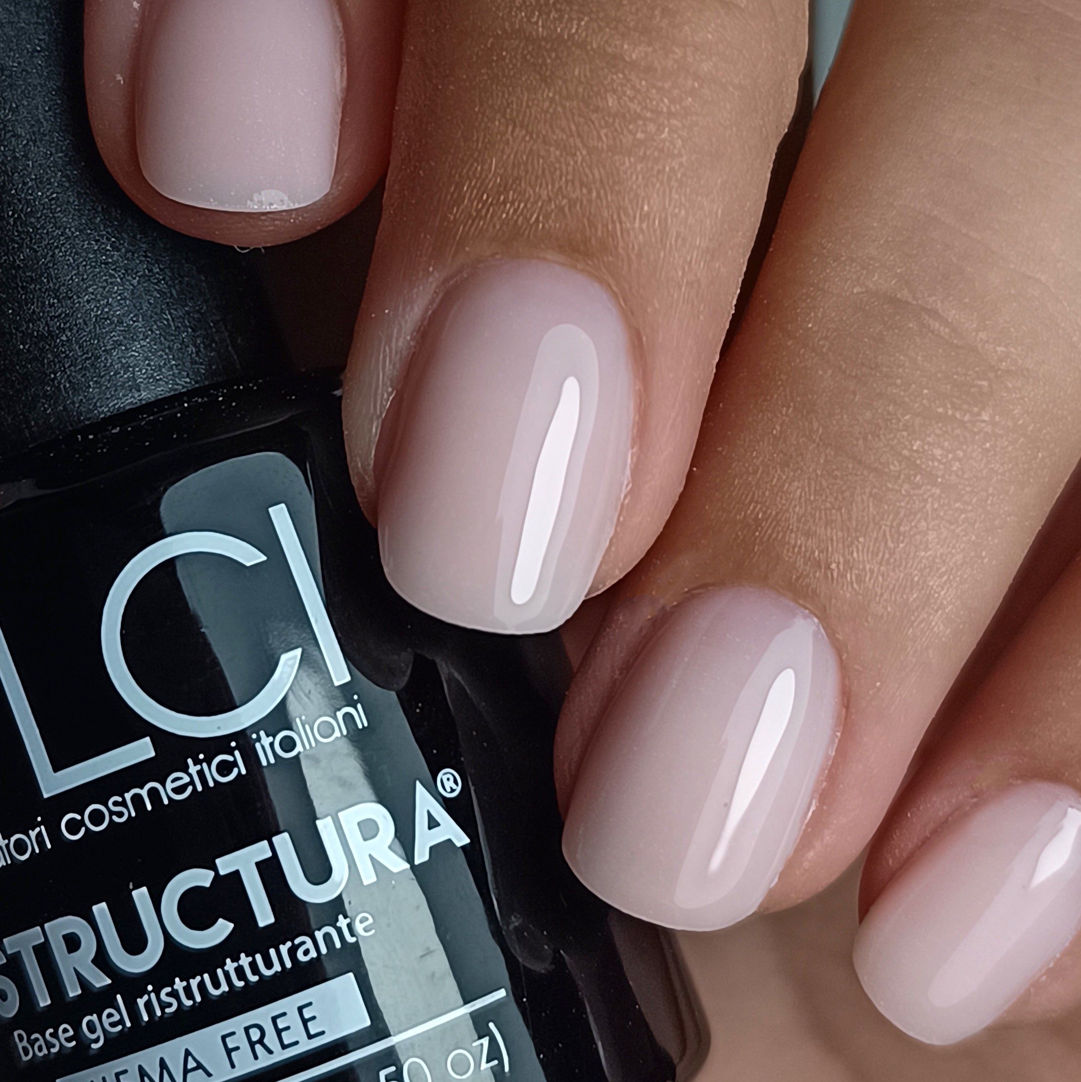 Primo piano di unghie smaltate. Accanto a un flacone nero con etichetta. Testo: LCI, Restructura, HEMA Free.