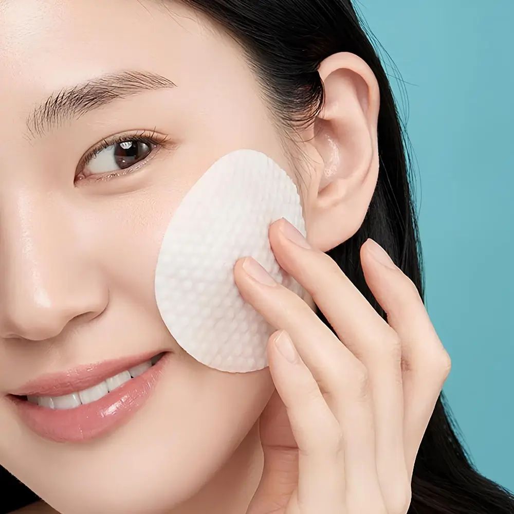 Pad viso ovale bianco strutturato. Donna tocca pad sulla guancia. Sfondo blu.