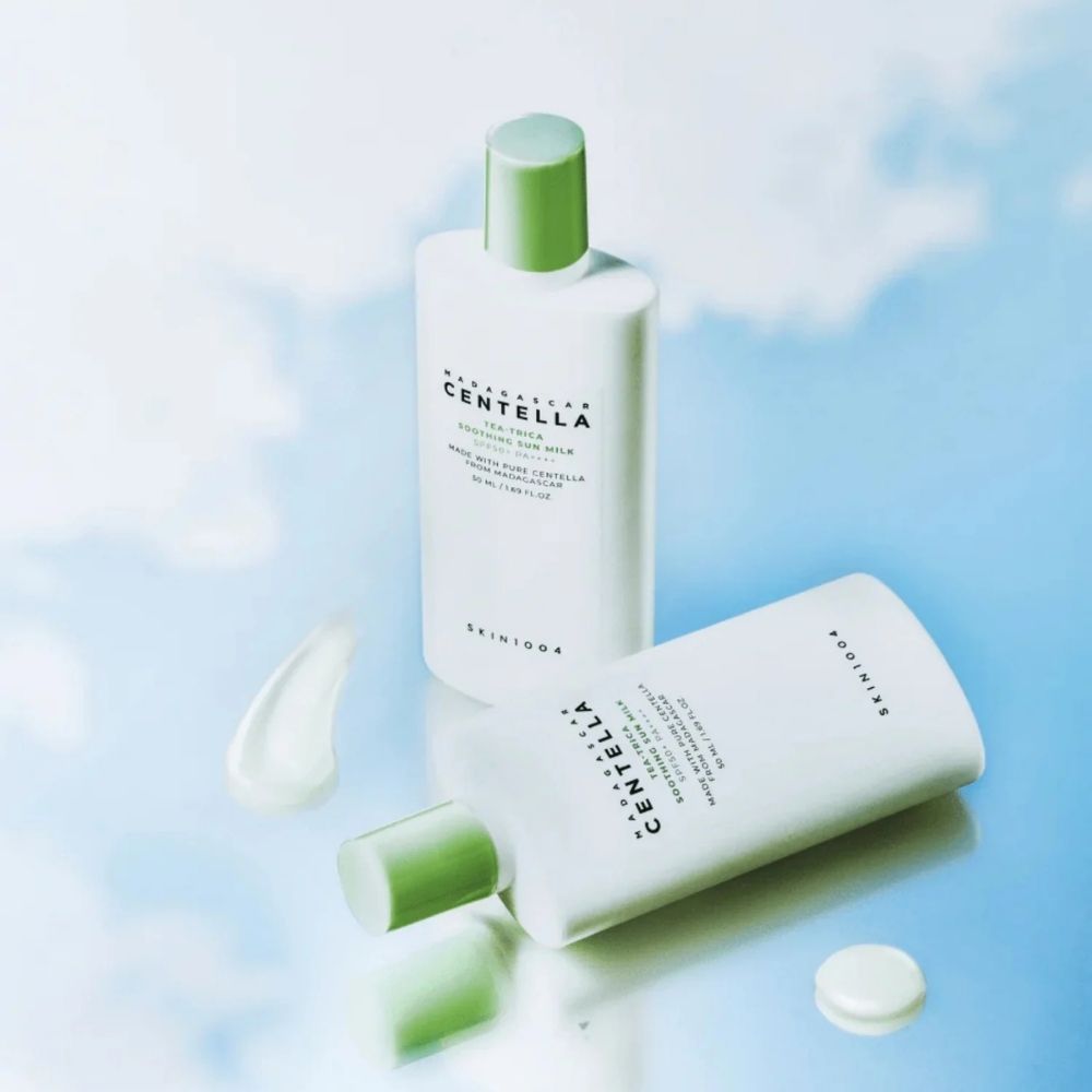 Due flaconi Madagascar Centella Tea-Trica Soothing Sun Milk SPF50+ PA++++, uno sdraiato, con campione di prodotto.