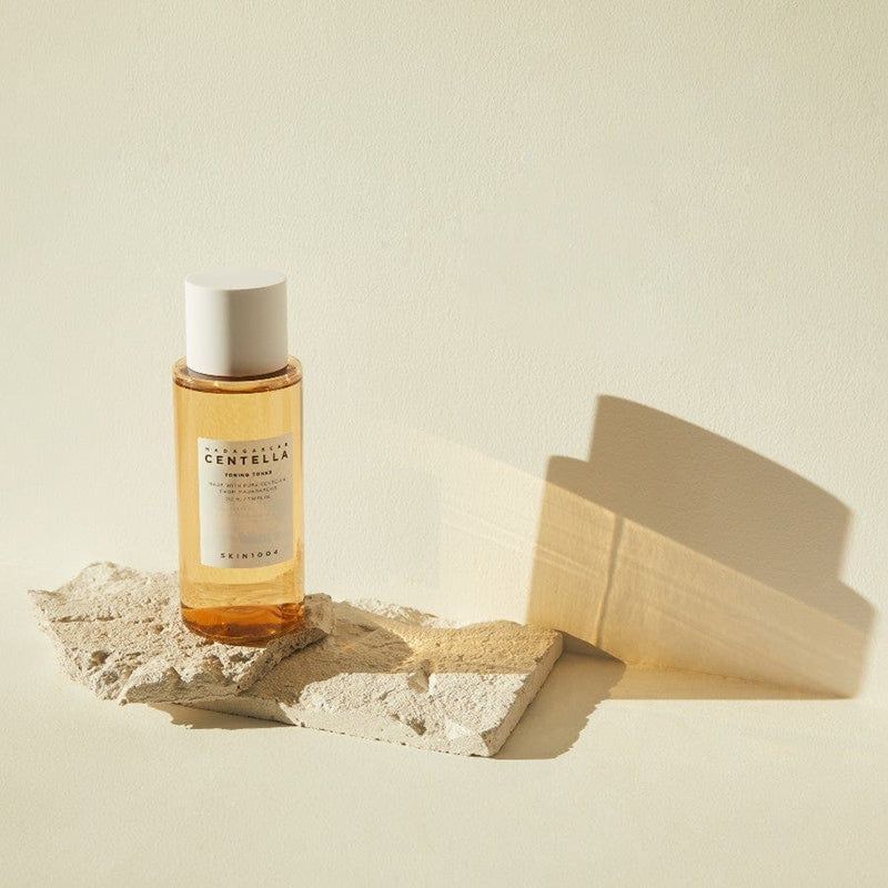 Una bottiglia su una pietra. Etichetta del prodotto con testo: MADAGASCAR CENTELLA TONING TONER. Tappo bianco.