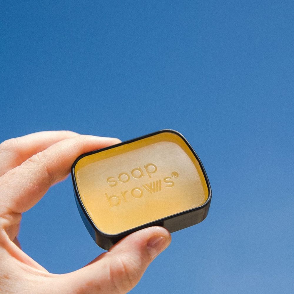 Mano che tiene un piccolo contenitore Soap Brows. Il nome del prodotto è impresso sulla superficie.