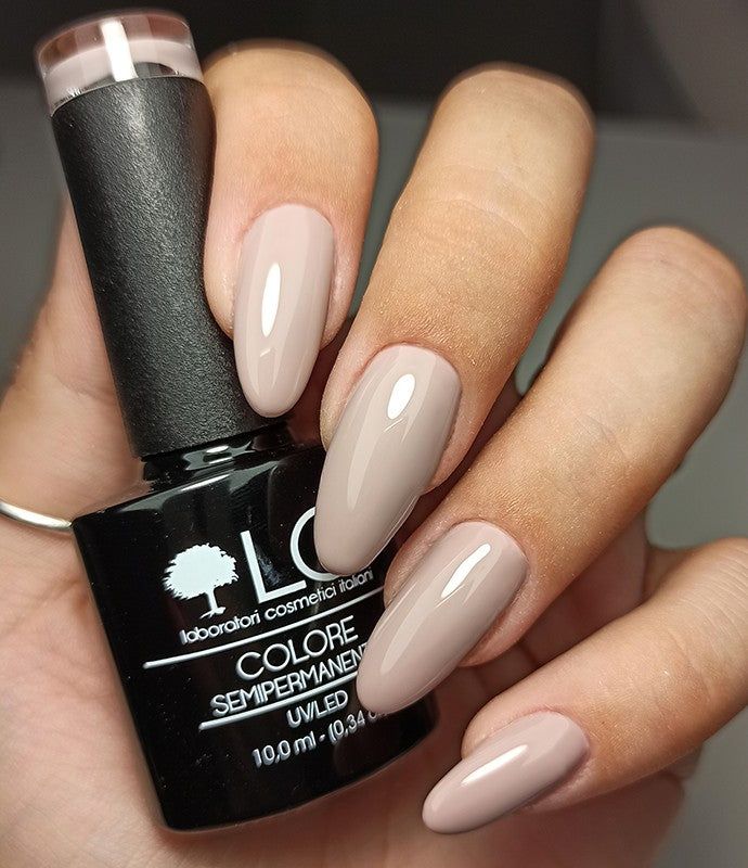 Mano con unghie smaltate e flacone smalto. Unghie color tortora chiaro, flacone con etichetta.