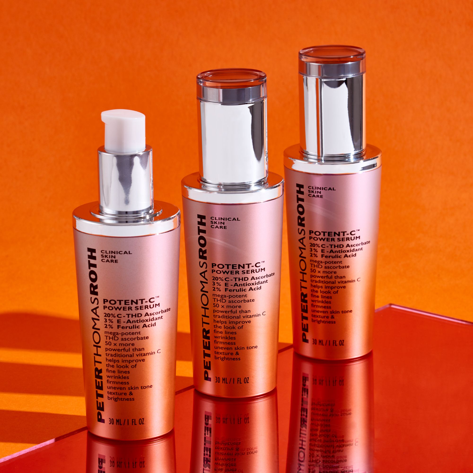Tre flaconi di siero. Scritta: Potent-C Power Serum. Tappi argentati e sfumatura arancione. Su sfondo arancione.