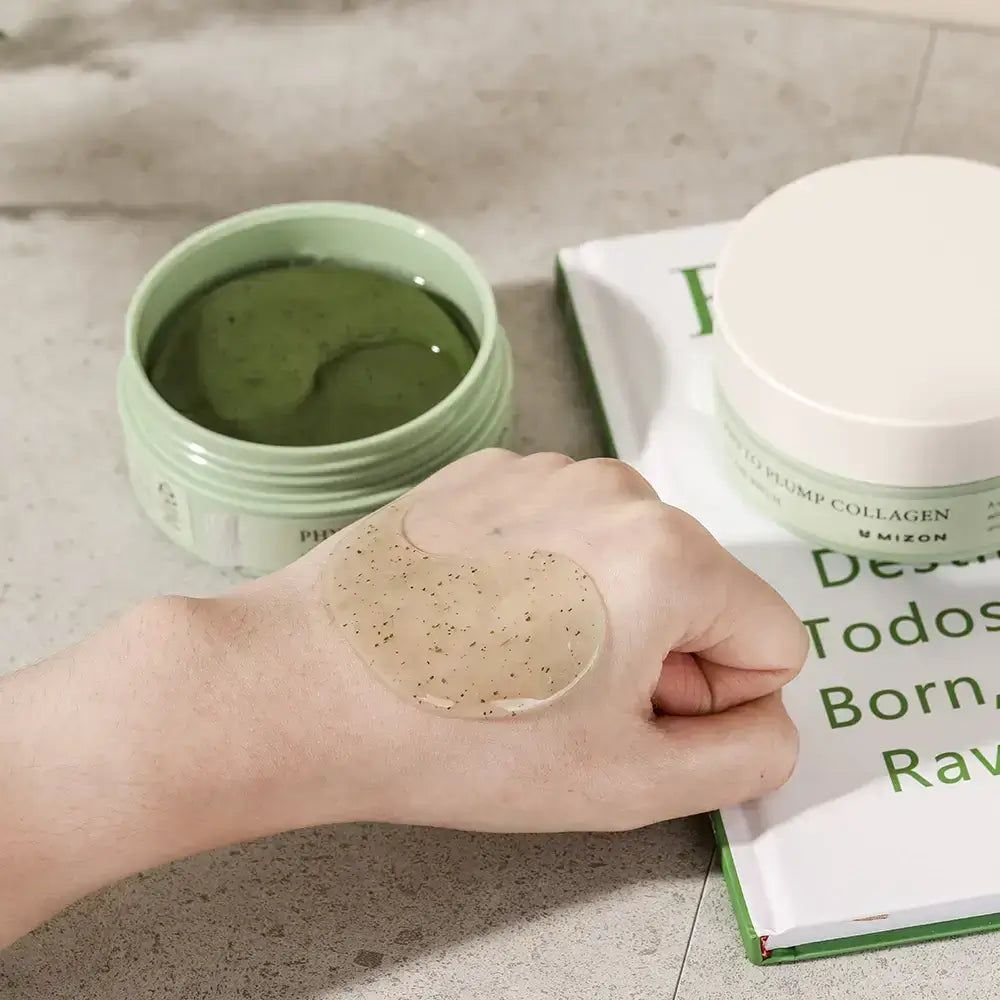 Vasetto aperto con patch in gel per occhi. Gel sulla mano. Scritta: Phyto Plump Collagen Eye Gel Patch. Marchio: Mizon. Libro sullo sfondo.