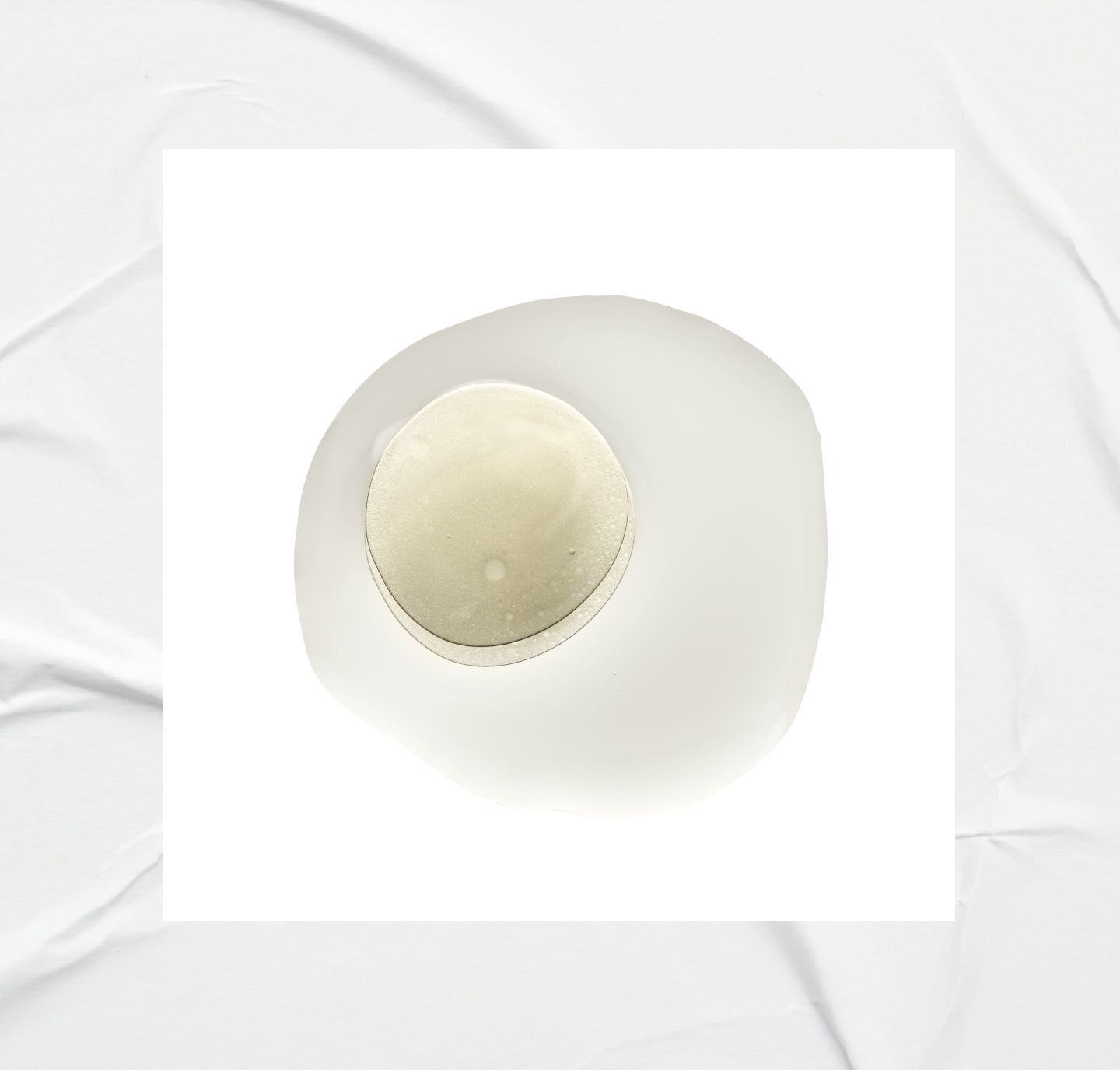 Sfondo bianco con una goccia di liquido e un oggetto rotondo al centro.