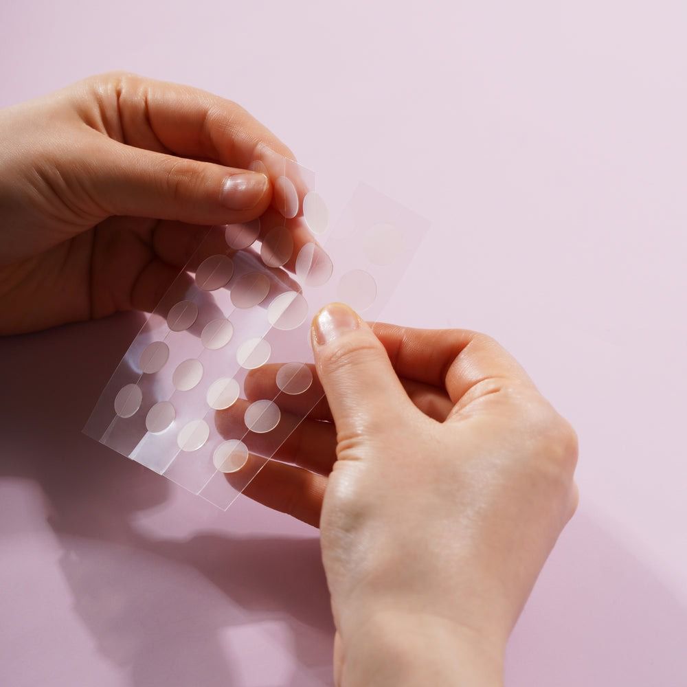 Mani che tengono un foglio di cerotti rotondi e trasparenti. I cerotti vengono rimossi dal foglio.