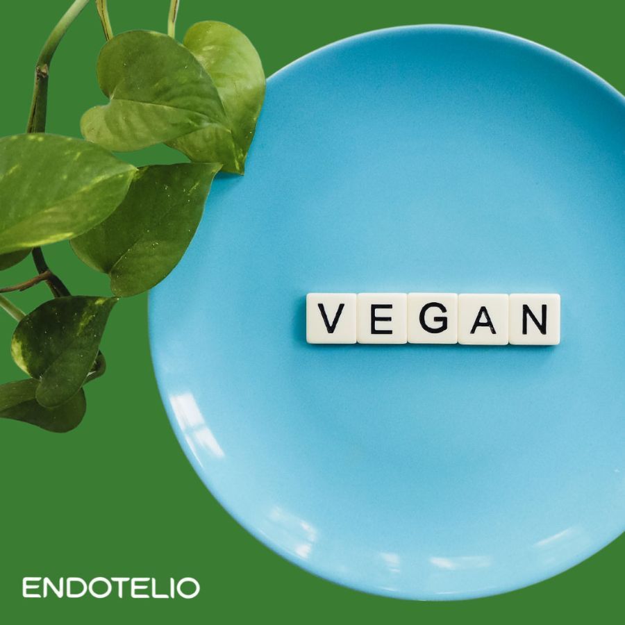Piatto blu con la parola 'VEGAN' in lettere bianche. Sfondo verde. Logo Endotelio in basso a sinistra.