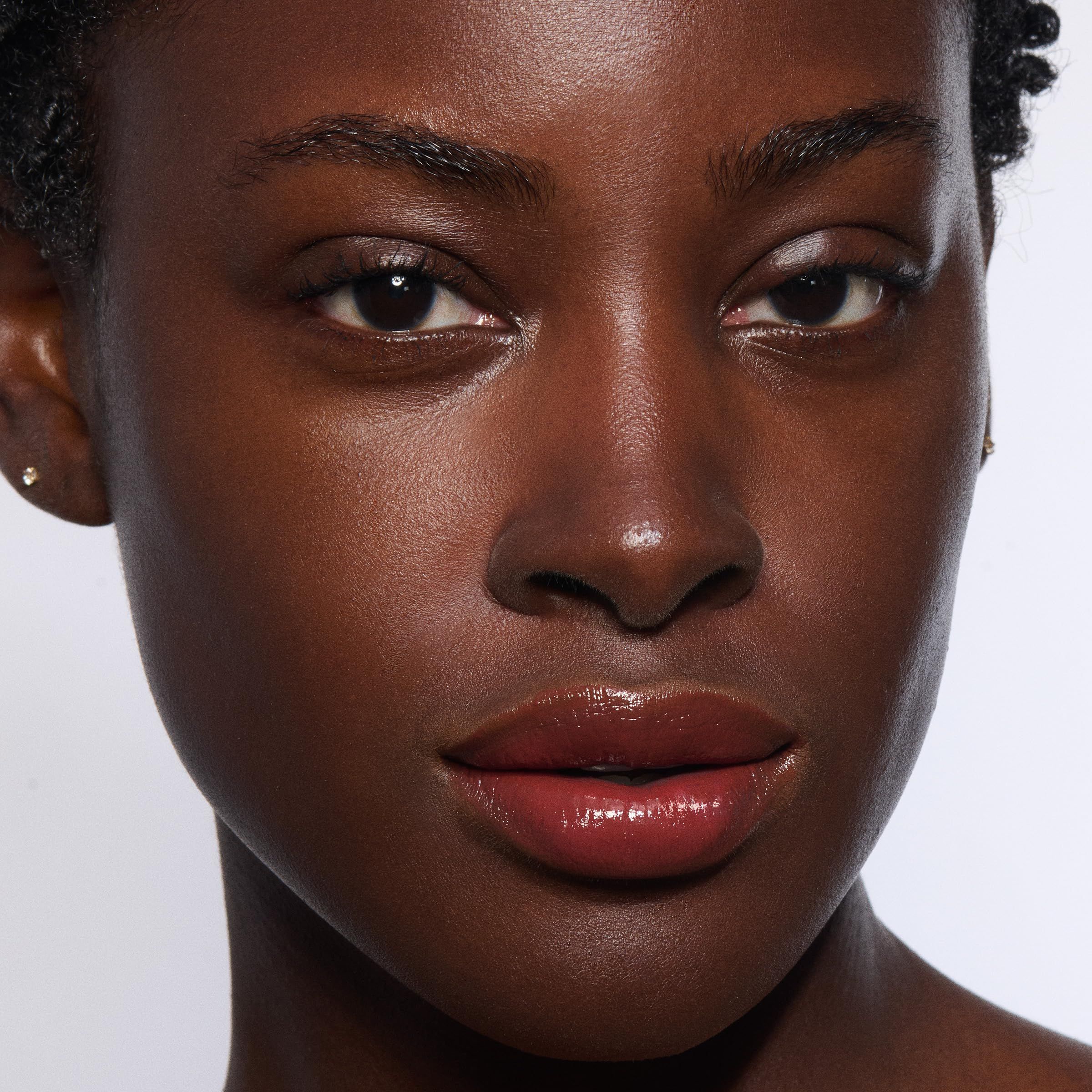 Primo piano di un viso con rossetto. Pelle scura, labbra con Lip Oil Balm. Nessun nome di prodotto visibile.
