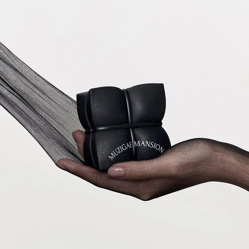Prodotto quadrato nero con logo MUZIGAE MANSION, tenuto in mano.