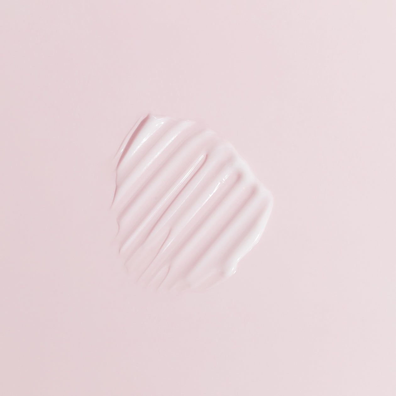 Campione di crema rosa con texture a coste su sfondo rosa. Prodotto per pelli sensibili.