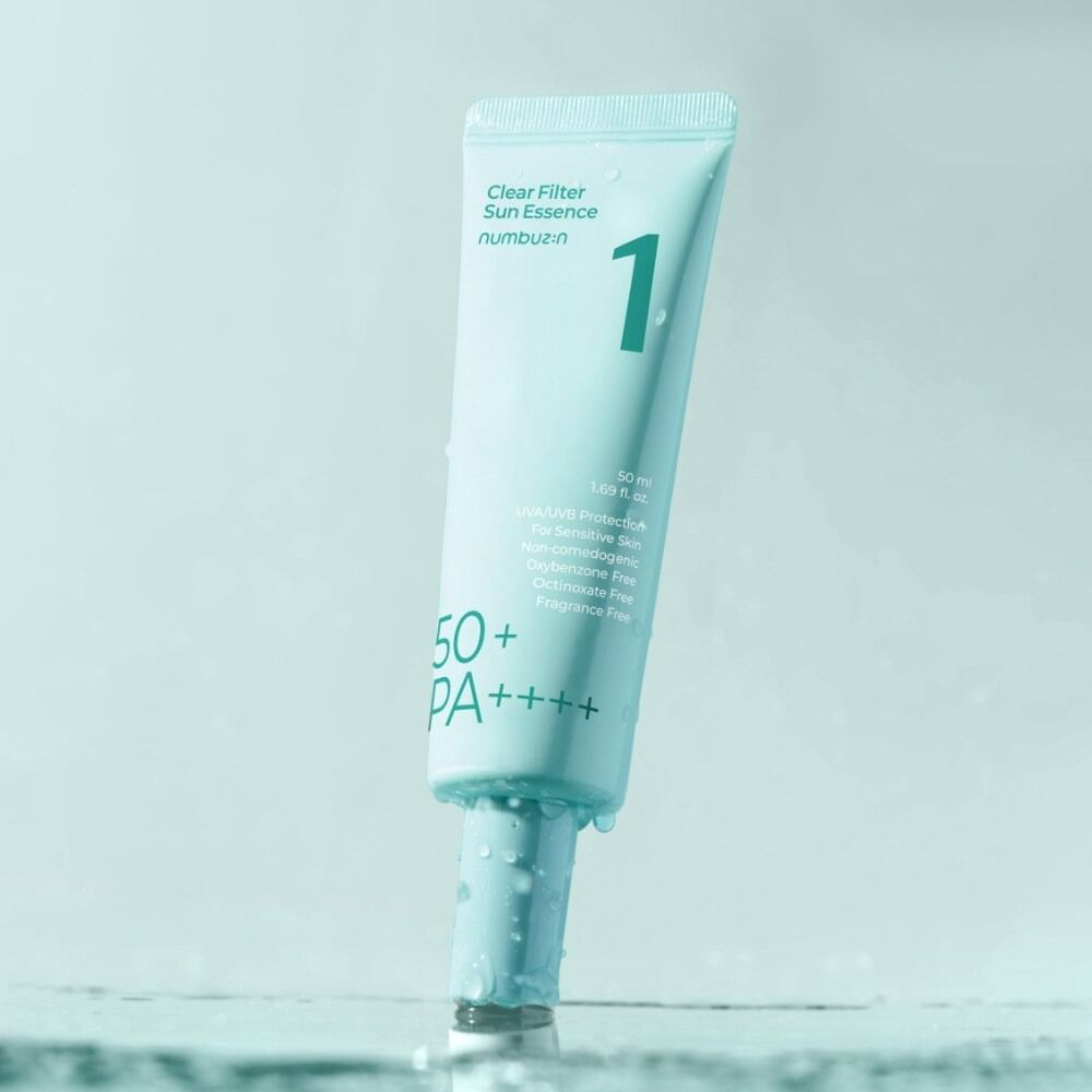 Tubo azzurro chiaro con nome del prodotto e SPF50+. Gocce sul tubo. Nome del prodotto: Clear Filter Sun Essence.