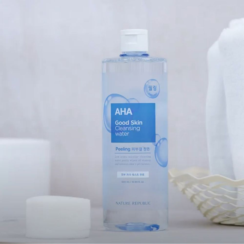 Flacone trasparente con etichetta blu. Scritta: AHA Good Skin Cleansing Water. Marchio: NATURE REPUBLIC. Accanto a una spugna bianca e un asciugamano.