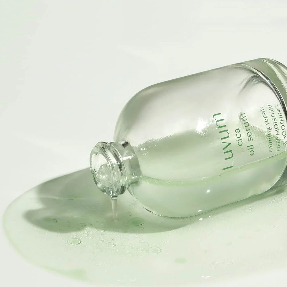 Flacone di siero appoggiato su una superficie. Il siero fuoriesce dal flacone. Scritta: Luvum cica oil serum. Testo: real calming repair, deep moisture & soothing.