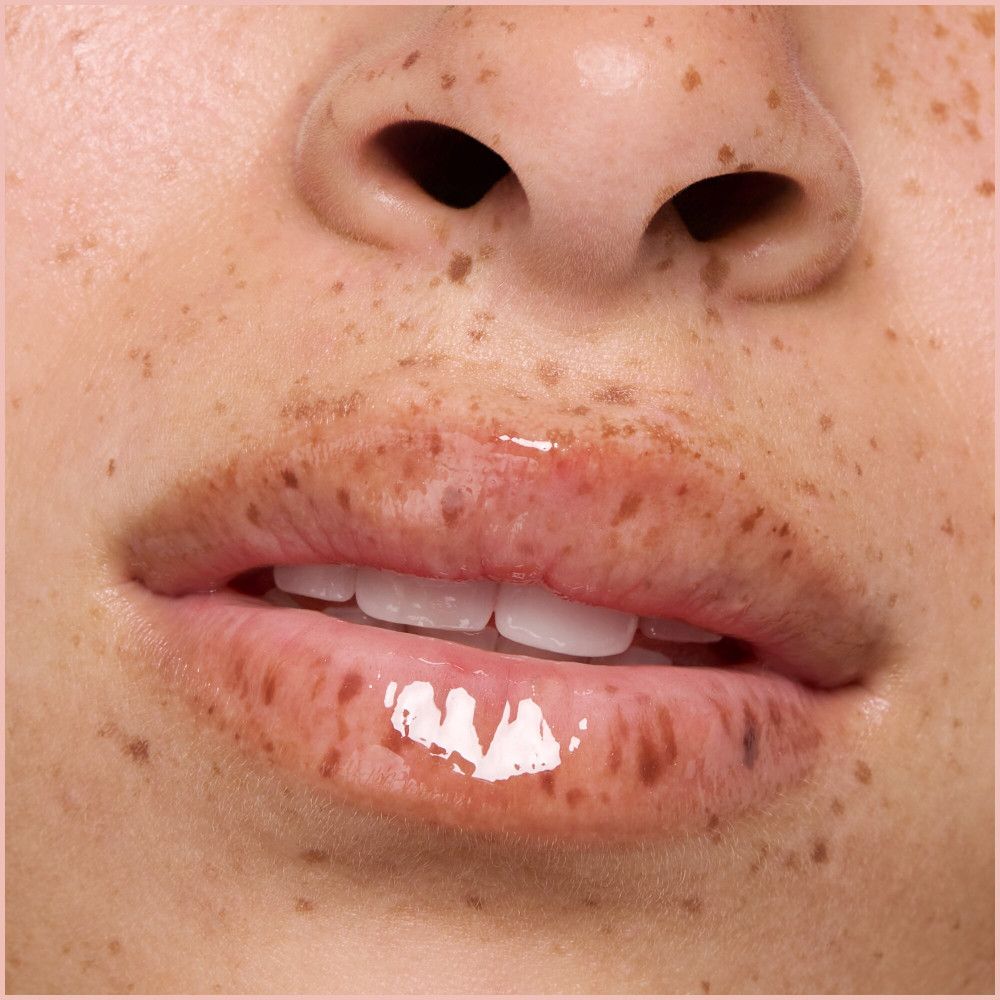 Primo piano di labbra con olio labbra lucido. Pelle con lentiggini.