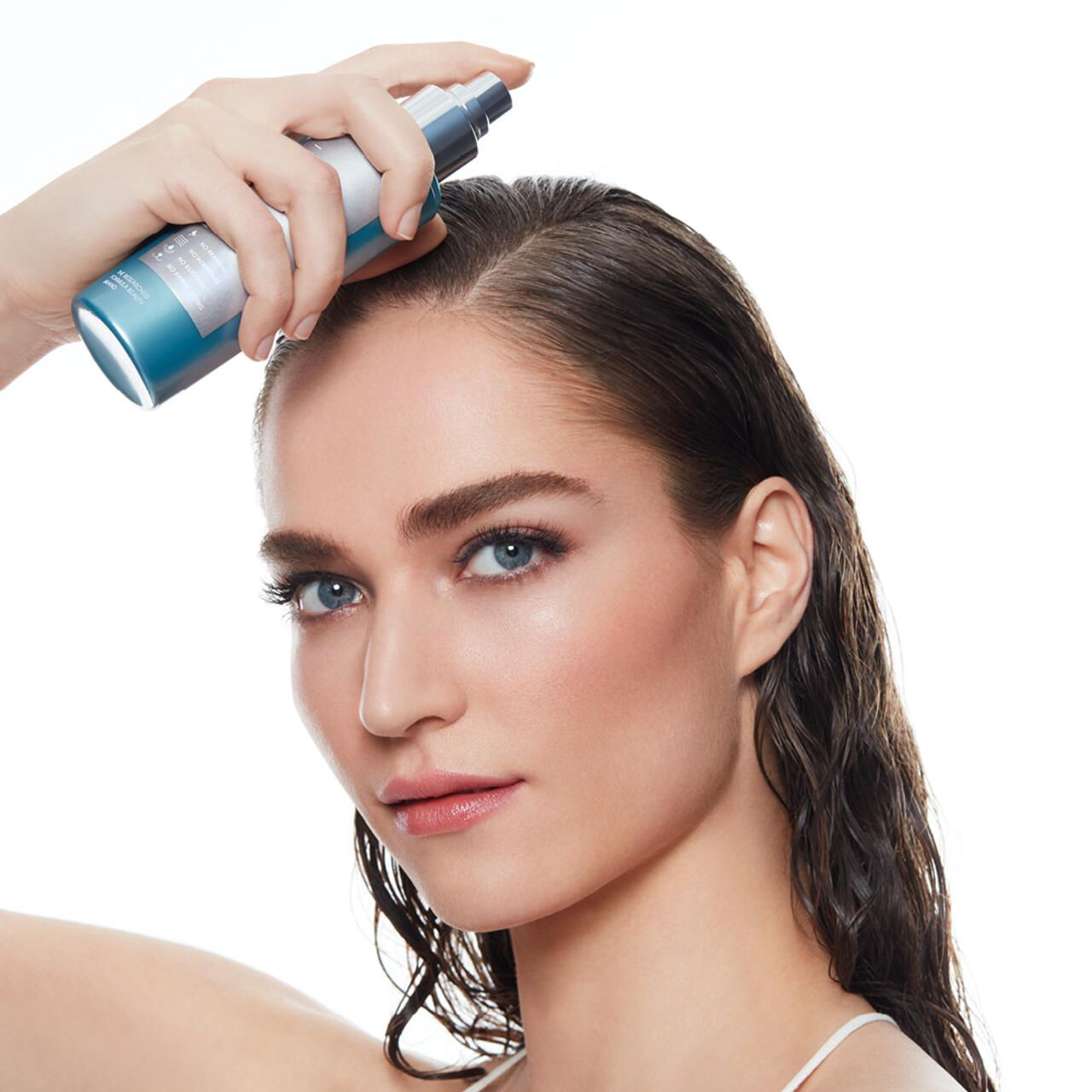 Donna che spruzza siero sui capelli. Flacone con vaporizzatore. Primo piano del viso, sfondo chiaro.