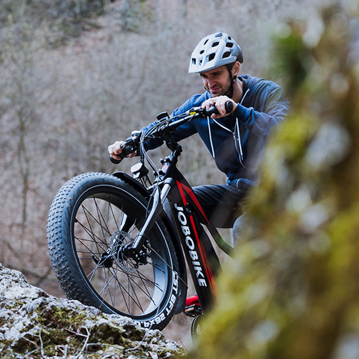 Persona su una e-bike JOBOBIKE Robin. Guida su un sentiero roccioso. Casco e natura sullo sfondo.