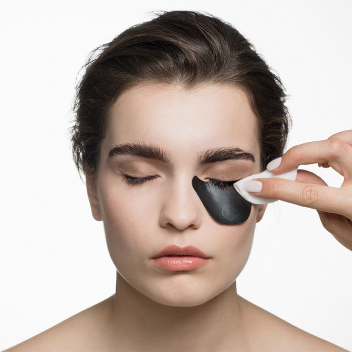 Viso di donna con patch occhi. Una mano tiene un batuffolo di cotone. Occhi chiusi.