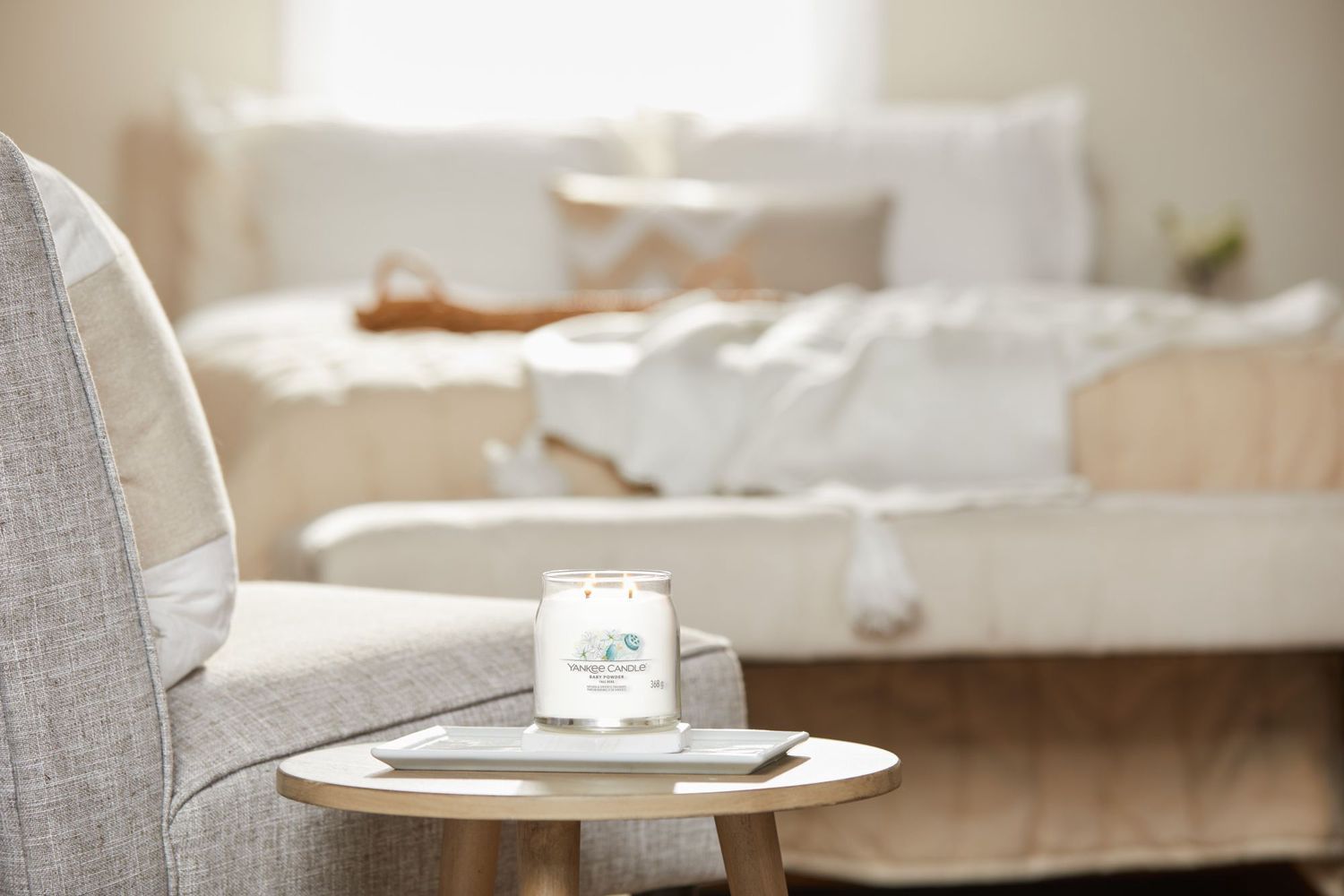 Candela su un tavolino. Un letto sullo sfondo. Etichetta con fiori e testo: Yankee Candle Baby Powder.