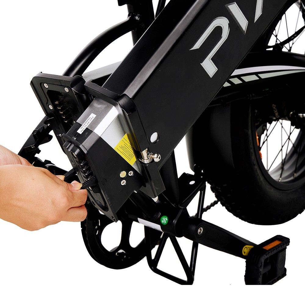 Primo piano della bici elettrica. Mano collega il cavo alla batteria. Pedali e telaio visibili.