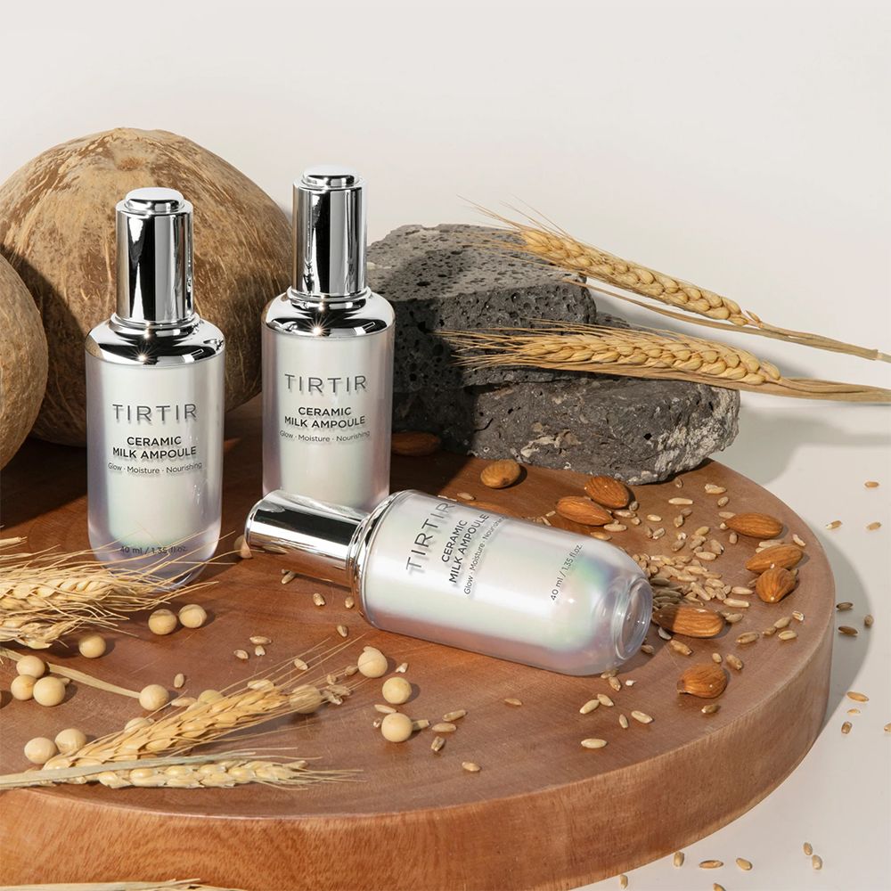 Tre ampolle TIRTIR Ceramic Milk su tavola legno. Testo: Glow, Moisture, Nourishing. Decorazioni: cereali, noci, cocco.