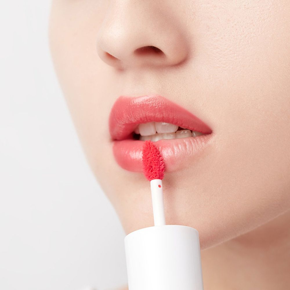 Labbra con lucentezza colorata. Viene utilizzato un applicatore con spugna rossa. Il rossetto è bianco.