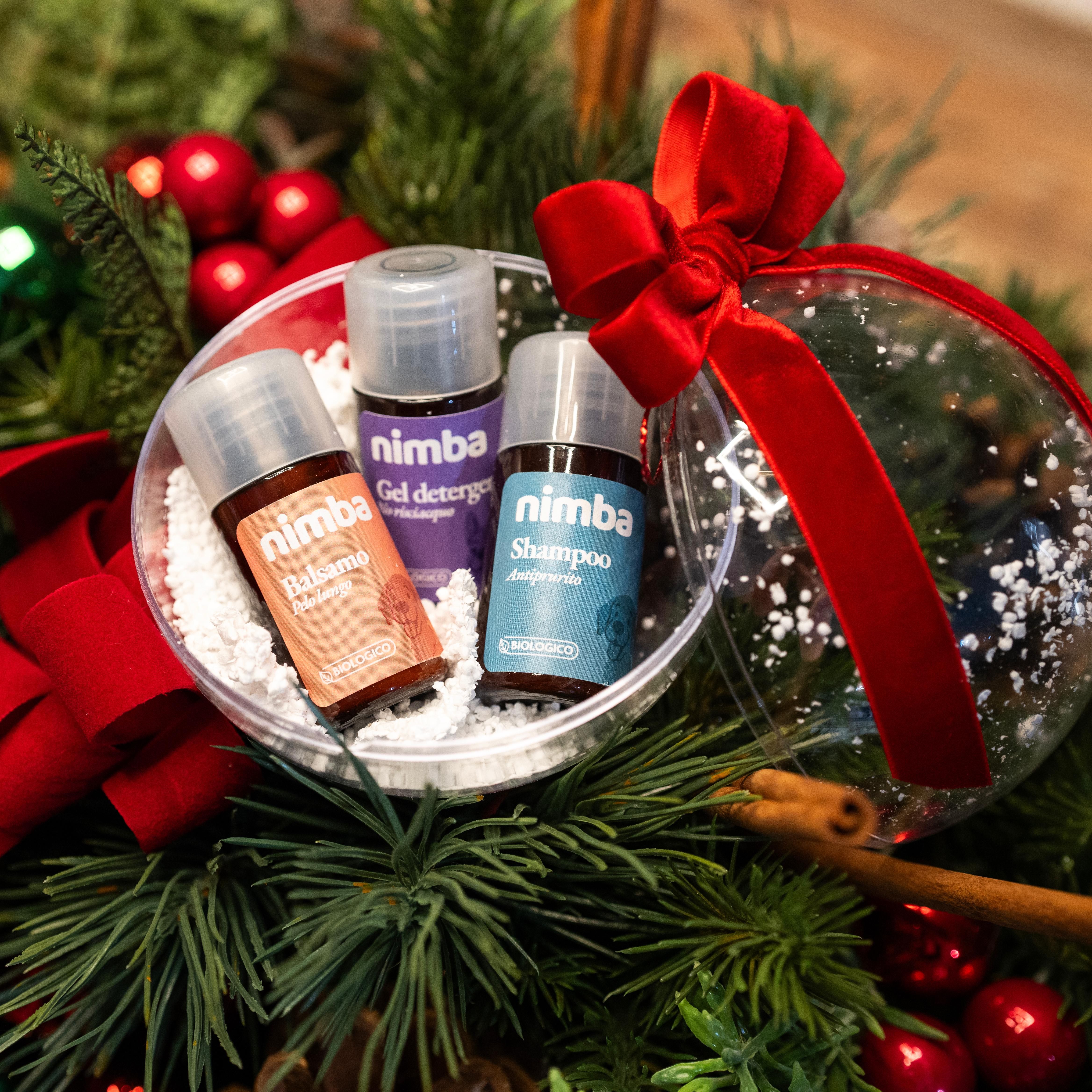Tre piccole bottiglie in una sfera trasparente, circondate da rami di pino e un fiocco rosso. Su ogni bottiglia c'è scritto « nimba ».